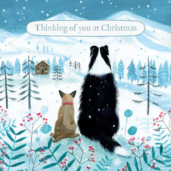 Two dogs sitting in a snowy landscape with trees and a cabin, accompanied by the text 'Thinking of you at Christmas'.