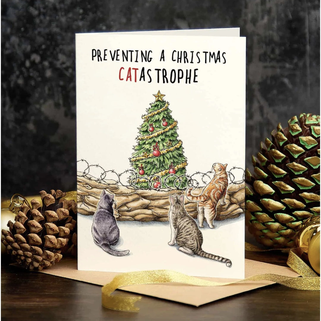 Card with cats and a Christmas tree, text 'Preventing a Christmas Catastrophe', surrounded by pinecones and a gold bow.