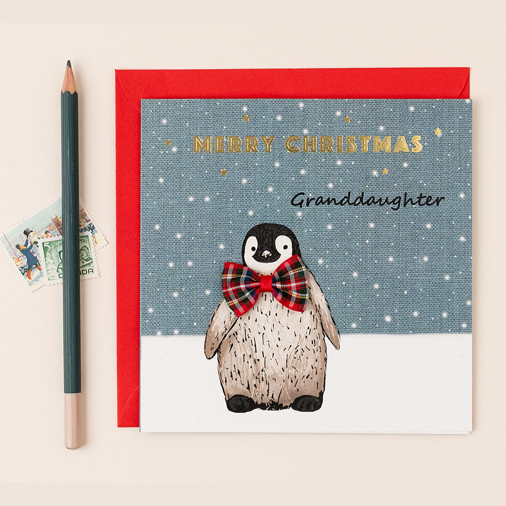 Christmas card with a penguin wearing a bow tie, addressed to a granddaughter, on a beige background.