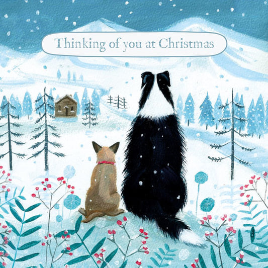 Two dogs sitting in a snowy landscape with trees and a cabin, accompanied by the text 'Thinking of you at Christmas'.