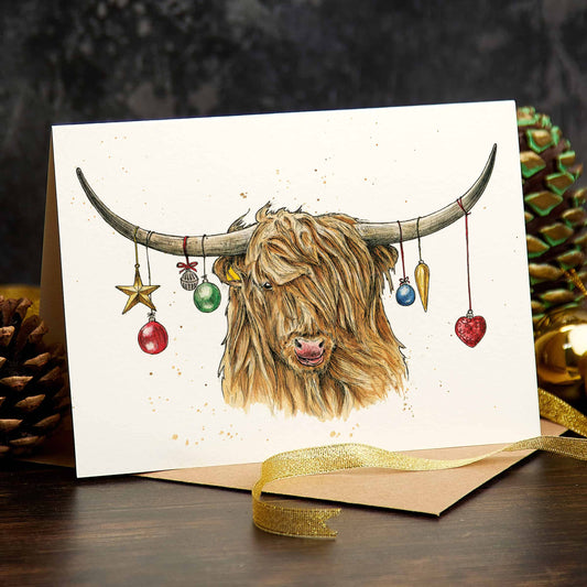 Greeting card with a highland cow illustration and Christmas ornaments, surrounded by festive decorations.