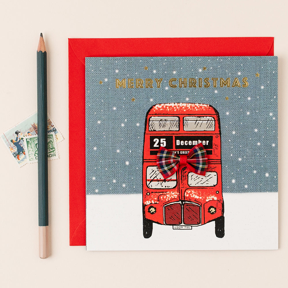 Christmas card with red London bus illustration and 'Merry Christmas' text on a textured background.