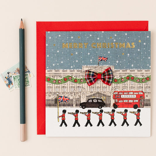Christmas card with a festive design featuring a London scene, including a red double-decker bus and a marching band, with a red envelope.